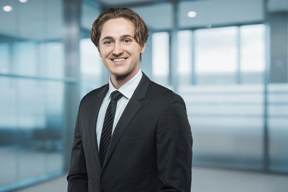 Bewerbungsfoto eines jungen Mannes im Anzug vor heller Glasfassade