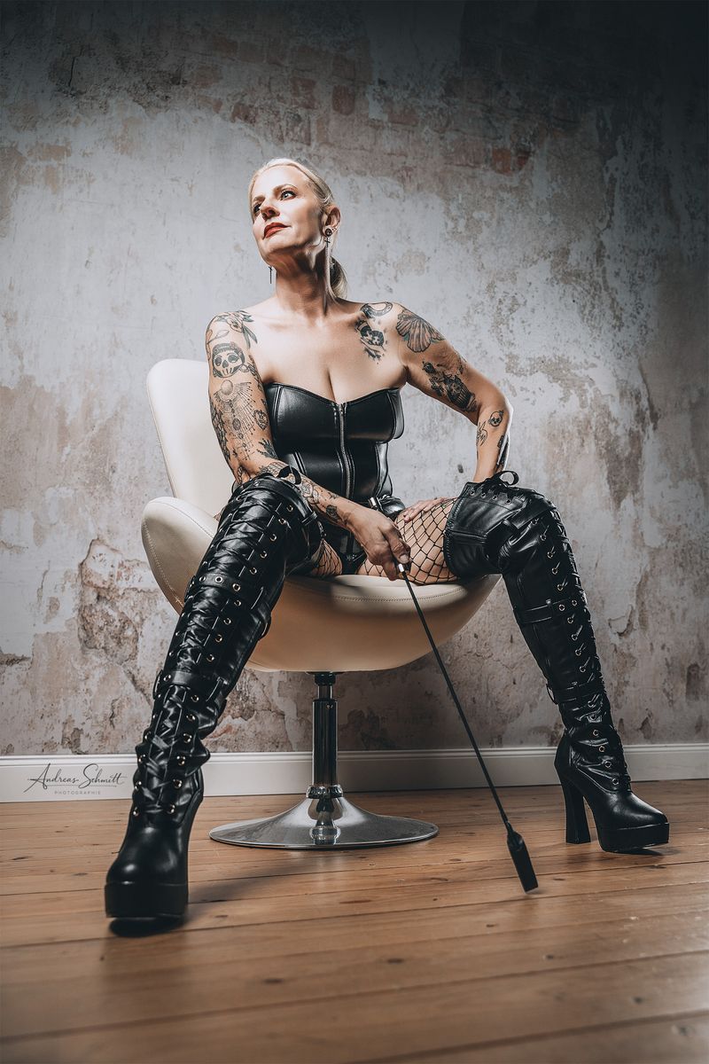 Domina in einer dominanten Pose sitzend im Studio