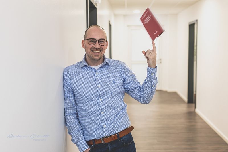 Mann im blauen Hemd hält einen roten Ordner im Flur