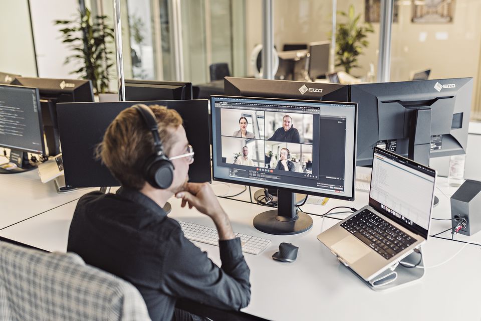 Mitarbeiterin mit Headset in einer Videokonferenz am Schreibtisch
