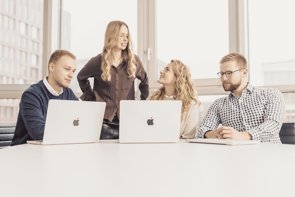 Vier Kolleginnen und Kollegen im Gespräch am Tisch mit Laptops